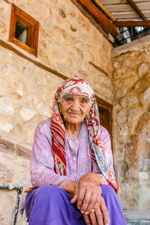 Unidentified old Turkish Muslim woman poses for camera in front of an old stone house in...