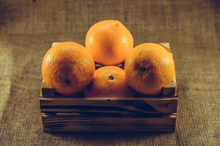 Fresh ripe orange fruits in old burnt wooden crate or box with sackcloth background.Vintage and retro effect added.の写真素材
