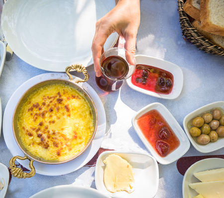 Top view of traditional Turkish breakfast with different food on a wooden table at outside,a picnic area.Woman hand holding tea glass to drinkの写真素材