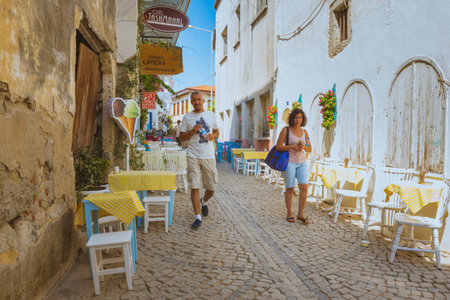 Unidentified People walk at a street with cafe and restaurant with tables and chairs  around at Alacati Town,a popular destination for traveling and vacation in Izmir,Turkey.26 August 2017.のeditorial素材