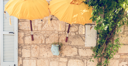 View of a white color opened wooden window with yellow umbrellas for decoration and green plants nearside.Ancient white stone wall on the background.の写真素材