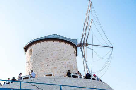 People eating and drinking at a cafe near windmill on a sunny day in Alacati town, a popular destination for traveling and holiday in Izmir,Turkey.26 August 2017.のeditorial素材