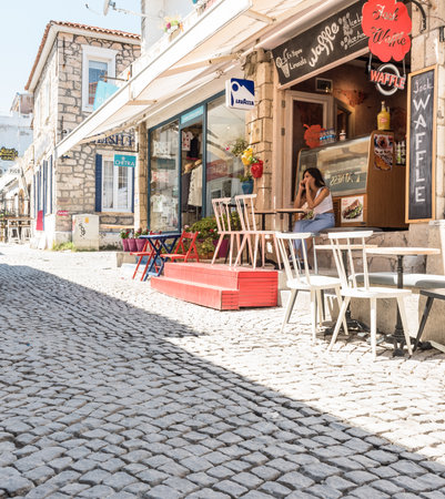 Unidentified woman talking on phone at a cafe with tables and chairs around at Alacati Town,a popular destination for traveling and vacation in Izmir,Turkey.26 August 2017.のeditorial素材