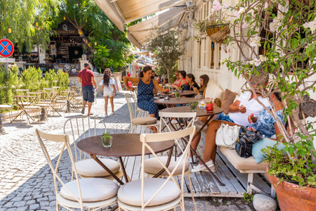 Unidentified People enjoying time at a street cafe with tables and chairs  around at Alacati Town,a popular destination for traveling and vacation in Izmir,Turkey.26 August 2017.のeditorial素材