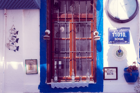 Colorful Decorations hanging on a white stone wall with blue window and different kind of ornaments in Alacati,Turkey.のeditorial素材