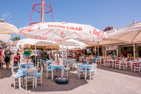 Unidentified People walk at a street with cafe and restaurant with tables and chairs  around at Alacati Town,a popular destination for traveling and vacation in Izmir,Turkey.26 August 2017.のeditorial素材