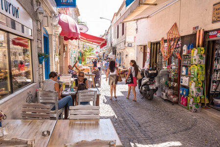 Unidentified People walk at a street with cafe and restaurant with tables and chairs  around at Alacati Town,a popular destination for traveling and vacation in Izmir,Turkey.26 August 2017.のeditorial素材