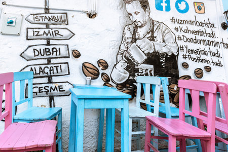 Retro Photo Filter Effect-View of wooden blue table and pink chairs with paintings on the wall at Alacati charming Streets , a popular destination for traveling and vacation in Izmir,Turkey.26 August 2017.のeditorial素材