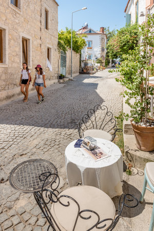 Unidentified People walk at a street with cafe and restaurant with tables and chairs  around at Alacati Town,a popular destination for traveling and vacation in Izmir,Turkey.26 August 2017.のeditorial素材