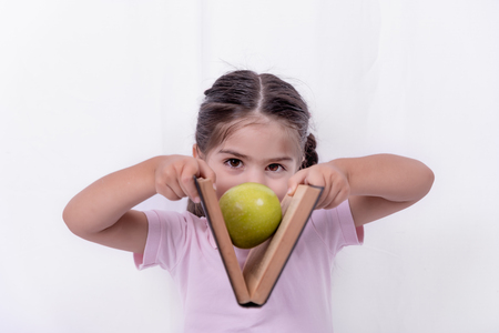 Cute little happy girl in school uniform holds a book with apple between pages.Selective focus and small depth of field.の写真素材