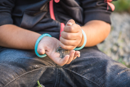 Close view of little girl hands while playing on ground with soul or small stones.の写真素材