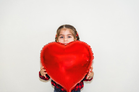 Adorable lovely little girl holds red heart shaped balloon.Holiday concept with isolated backgroundの写真素材