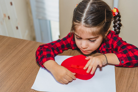 Adorable lovely little girl hold two small little thematic red shapes close eyes.Holiday concept with isolated background.の写真素材