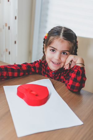 Adorable lovely little girl smiles camera before draw red heart shape over white paper.Holiday concept with isolated background.の写真素材