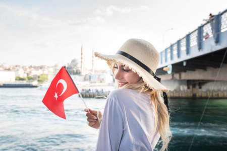 Attractive young beautiful girl waves Turkish flag over Galata Bridge and enjoys view of bosphorus...