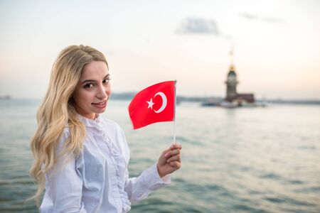 Attractive young beautiful girl waves Turkish flag and enjoys sunset view of bosphorus and Maiden Tower in Istanbul,Turkey.Travel Conceptの写真素材