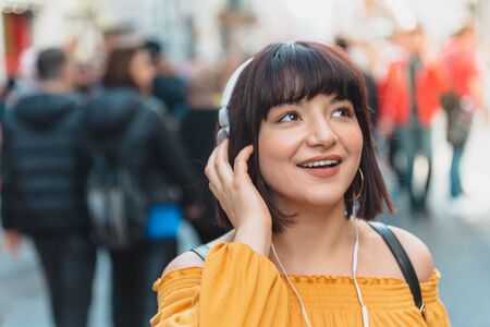 Beautiful young girl in fashionable clothes listen music at street while big smilingの写真素材
