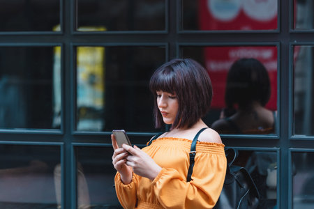 Beautiful young girl in fashionable clothes uses smartphone with black background windows while...
