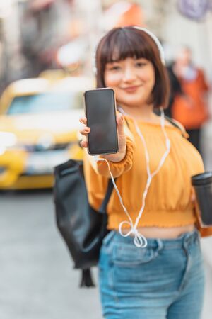 Portrait of smiling woman holding phone with blank screen to copy text or promotional Content at streetの写真素材