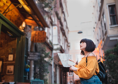 Beautiful young girl in fashionable clothes with map walks around city and looks around.Traveler...