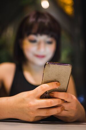 Close view of beautiful young girl in black dress chats with smart phone in a cafe or bar at night.の写真素材