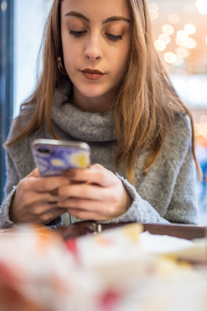Close view of beautiful young girl in jumper chats with smart phone in a cafe or restaurant.