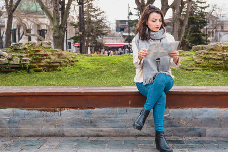 Beautiful young girl in fashionable clothes sits and looks at map in Istanbul,Turkey.Traveler woman ...