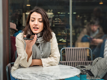 Attractive young beautiful girl holds phone and speaks activate virtual digital voice assistant on...