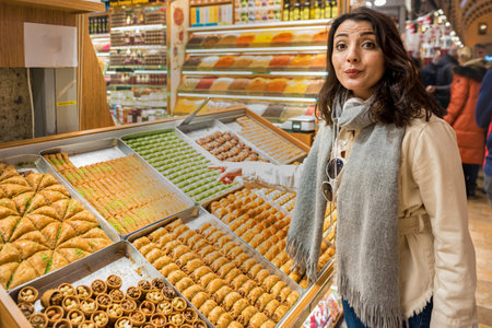 Beautiful traveler woman looks at traditional Turkish dessert Baklava sold in Egyptian bazaar in...