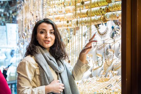 Beautiful woman in fashionable modern clothes looks at Gold jewelry shop stall store in grand Bazaar,Istanbul,Turkey.Modern women lifestyle or travel tourist conceptの写真素材