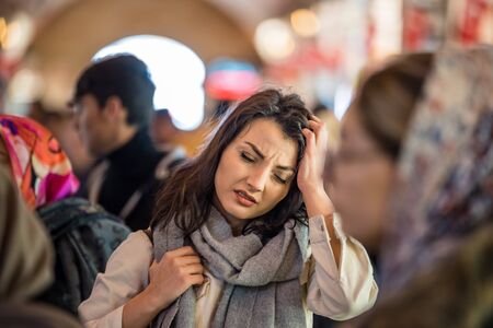 Beautiful woman in fashionable modern clothes suffers migraine or headache problem while standing crowd of people at road.の写真素材