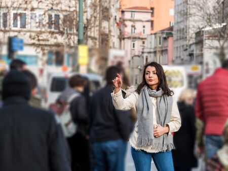 Beautiful young girl traveler in trendy casual wear raises her  hand to call a taxi while standing on road in city on urban background in waving on avenueの写真素材