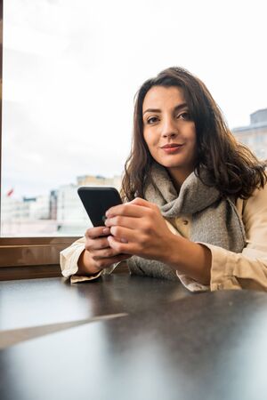Attractive young beautiful girl uses smart phone while sitting at a cafe.Woman Lifestyle technology conceptの写真素材