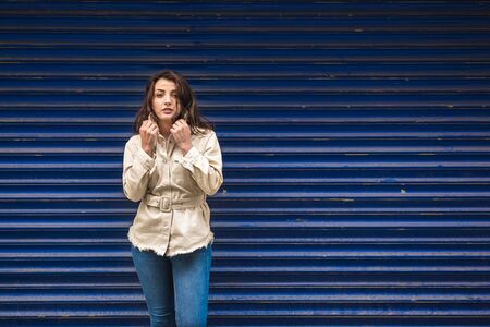 Beautiful young girl in fashionable clothes holds hand on collar of her grey coat and looking at camera.の写真素材