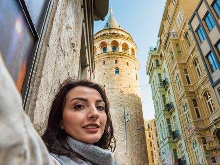 Beautiful young girl in fashionable clothes has selfie with view of landmark Galata tower in Beyoglu,Istanbul,Turkeyの写真素材