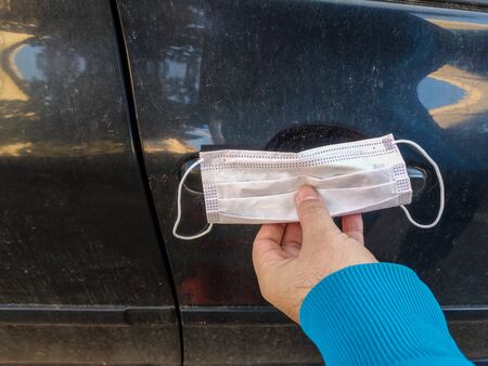 Close up of hand holding single use protective mask to open car door.Door handle of a black car.Anti bacterial and Corona virus (COVID-19)の写真素材