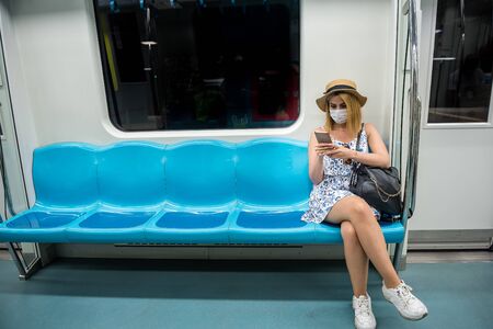 Young beautiful woman wears face mask and keeps social distance by sitting alone while transporting at train during covid-19 or coronavirus outbreak .の写真素材