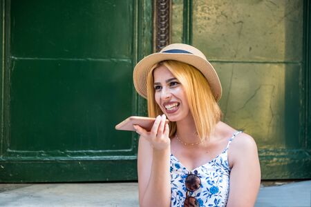 Young beautiful girl holds phone and speaks activate virtual digital voice assistant on smart phone.Woman uses smart phone voice recognition. Lifestyle technology conceptの写真素材
