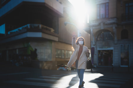 Beautiful girl wearing protective medical mask and fashionable clothes cross road,street. New normal lifestyle concept.の写真素材