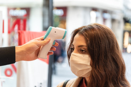 Man hand holding thermometer checks fever of customer that wearing protective mask before shopping at supermarket during covid-19 pandemic. New normal lifestyle concept.の写真素材
