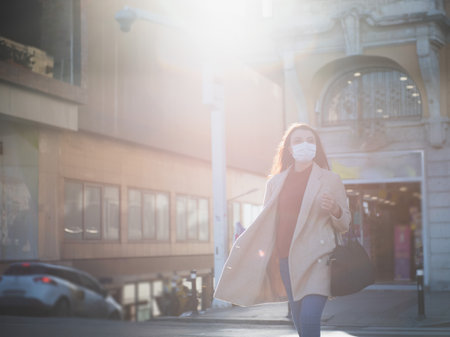 Beautiful girl wearing protective medical mask and fashionable clothes cross road,street. New normal lifestyle concept.の写真素材