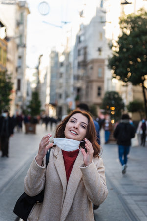 Beautiful girl in fashionable clothes holds and wears disposable mask at street. New normal lifestyle concept.の写真素材