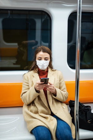 Beautiful woman wearing protective disposable mask keeps social distance and use smart phone by sitting alone while transporting.New normal lifestyle concept.の写真素材