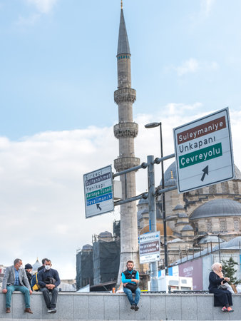 Unidentified Turkish people wearing protective face masks rest with view of New Mosque at Eminonu are while there is COVID-19 epidemic.Istanbul,Turkey.16 November 2020のeditorial素材