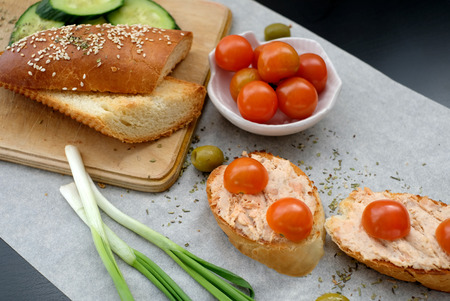 Top view of a crusty baguette slices with cherry tomatoes and green olives, cream cheese, healthy breakfast or snack on a wooden boardの写真素材