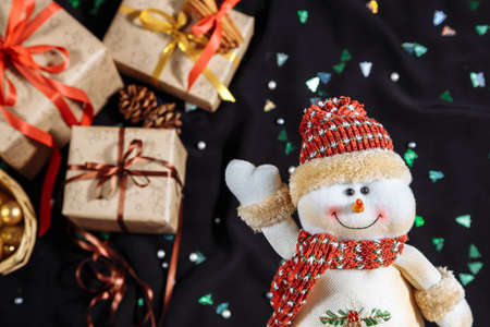 Cheerful snowman in red cap and scarf over blurred christmas gifts boxs with copy spaceの写真素材