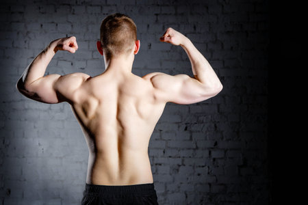 Rear view of young attractive caucasian muscular bodybuilder man with perfect body working out in...