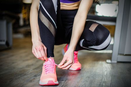 Young woman tying shoelaces before training in gymの写真素材