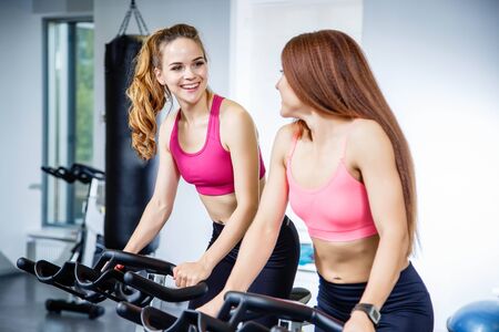 Two pretty women doing exercises on bicycles at the gymの写真素材