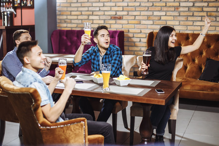 Happy friends having leisure in pub watching sport in TV together drinking beerの写真素材
